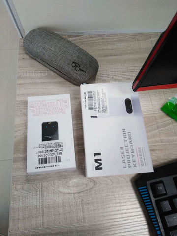 Virtual Laser Keyboard Bluetooth Wireless Projector packaging on a desk beside glasses case and keyboard.
